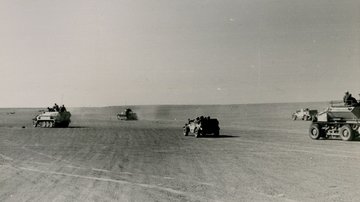 Mehrere Militärfahrzeuge fahren über eine sandige Ebene.