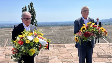 Zwei Männer mit Gestecken warten auf Kranzniederlegung