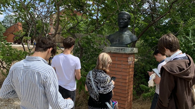 Jugendliche stehen vor einer Statue und lesen Hintergrundinfos auf ihren Smartphones.