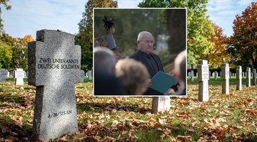 Mann bei Rede vor Publikum, im Hintergrund Soldatenfriedhof