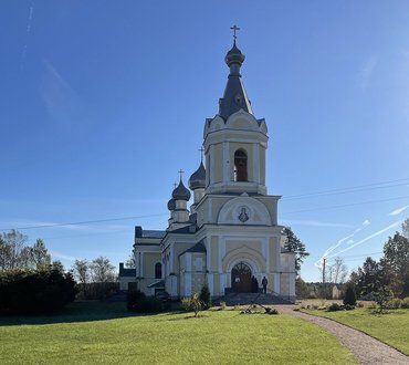 Kirche in den Farben Weiß und Gelb mit Zwiebelturm auf Rasenfläche