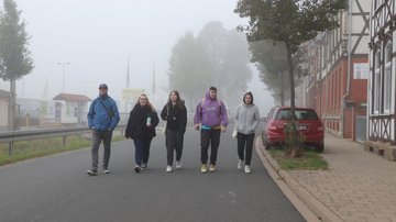 Fünf junge Menschen gehen nebeneinander auf einer Straße im Nebel.