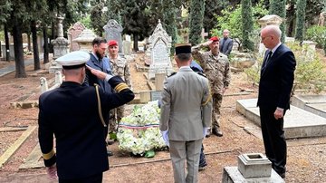 Männer stehen im Kreis um Kränze auf Friedhof