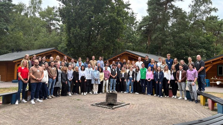 Gruppenfoto auf einem Platz vor Holzhütten