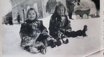 Schwarz-weiß-Foto: Zwei kleine Mädchen sitzen im Schnee.