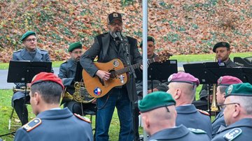 Mann spielt Gitarre, Soldaten im Hintergrund als Musiker, vorn als Publikum