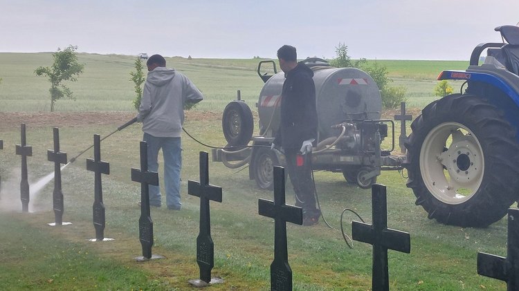 Zwei Jugendlichen säubern Grabkreuze mit Wasser aus kleinem Tankwagen