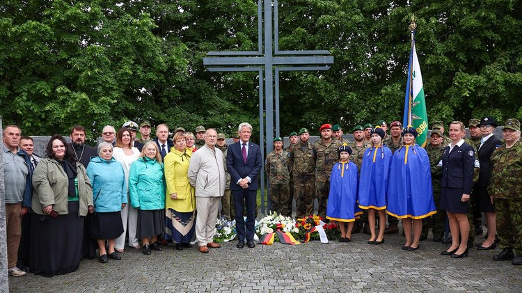 Frauen und Männer stehen links und rechts von einem Hochkreuz aus Metall