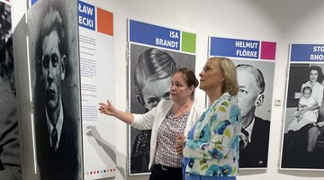 Zwei Frauen vor Tafeln mit Porträtfotos und Texten