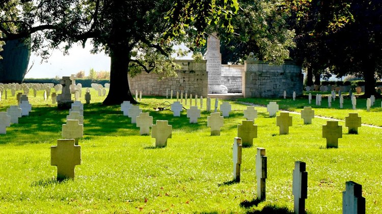 Ein Friedhof mit einheitlichen Grabkreuzen, im Hintergrund Bäume und ein Denkmal