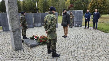 Männer gedenken der Toten, Soldaten stehen rechts und links der Gestecke am Hochkreuz