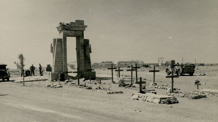 Man sieht die Ruine eines Tores, davor befinden sich mehrere Soldatengräber.