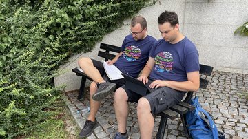 Zwei junge Männer mit Laptop und Papier auf einer Bank