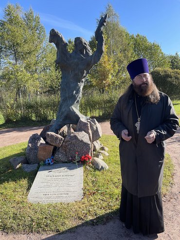 Geistlicher rechts vor Bronze-Skulptur auf Friedhof