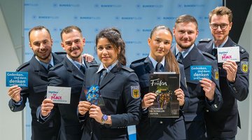 Sechs Menschen in Polizeiuniform halten Werbematerial Richtung Kamera