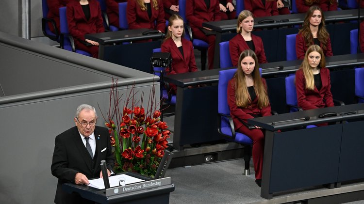 Mann am Rednerpult, junge Frauen im Hintergrund hören zu