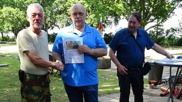Drei Männer, der Mittlere überreicht dem Linken eine Urkunde