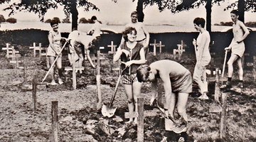 Junge Frauen und Männer stehen mit Spaten auf einem Friedhof.