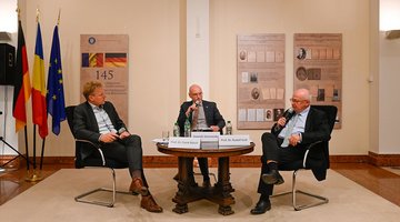 Drei Männer an einem Tisch, links drei Flaggen