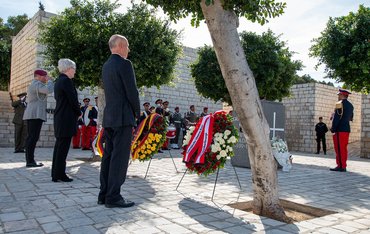 Ein Soldat, eine Frau, ein Mann stehen vor drei Gedenkkränzen
