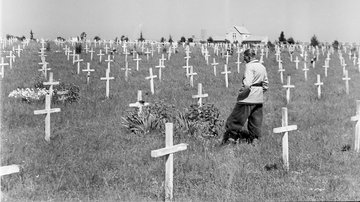 historisches Foto - Blick auf Gräberfeld mit weißen Kreuzen und einem Mann vor einem Kreuz