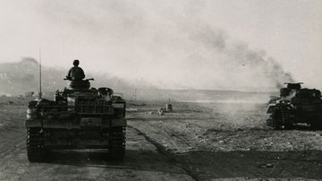 Ein Militärfahrzeug fährt an einem brennenden Panzer vorbei.