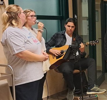 Zwei junge Frauen singen, junger Mann spielt Gitarre