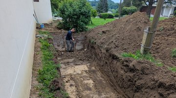 Tiefer Graben neben Gebäude, ein Mann arbeitet am Ende mit Spaten