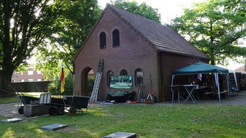 Haus, davor Arbeitsgerät, rechts ein mobiler Pavillon