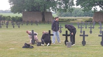 Vier Jugendliche säubern Grabkreuze auf einer Kriegsgräberstätte