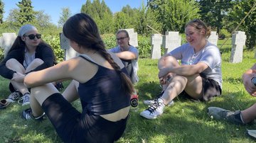 Junge Frauen sitzen auf der Wiese vor Grabsteinen