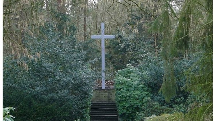 Der Blick geht auf der errichtete Hochkreuz, auf einer Terrasse, inmitteln von Bäumen und Büschen.