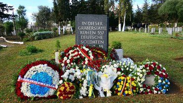 Mahnmal aus Stein mit zahlreichen Kränzen davor 