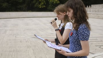 Zwei junge Frauen mit Clipboard und Mikrophon tragen etwas vor.