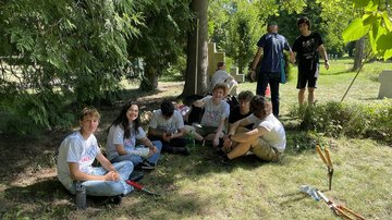 Gruppe junger Leute sitzt im Gras unter Bäumen