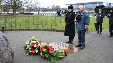 Mann und Frau stehen vor zwei Kränzen am Boden