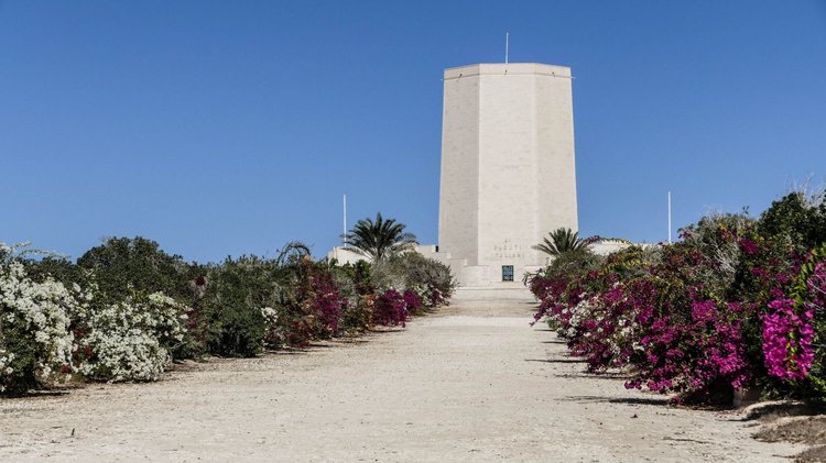 Ein breiter Turm vor blauem Himmel, Oleander und Palmen