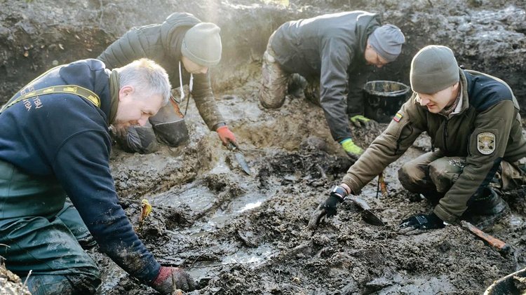 Vier Männer suchen in einer schlammigen Grube nach Knochen
