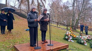 Zwei junge Menschen stehen vor Mikrophonen und lesen etwas vor.