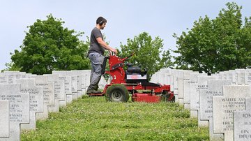 Mann steht auf Rasentrecker zwischen Grabkreuzen