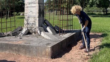 Frau reinigte Sandfläche an Denkmal mit Hacke
