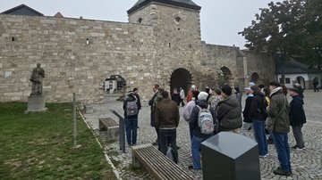 Junge Menschen stehen vor einer Stadtmauer.
