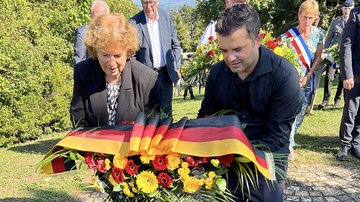 Frau und Mann legen Gesteck mit Schleife in den Deutschlandfarben nieder
