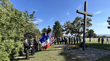 Menschen, zum Teil mit Fahnen, im Halbkreis um Hochkreuz auf einem Friedhof