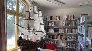 Blick in einen Raum mit Schiffsmodell und Regalen voller Bücher