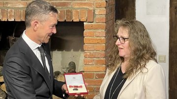 Ein Mann überreicht einer Frau eine Medaille in einem Kasten.